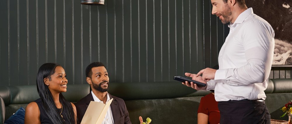 Un restaurateur consulte son téléphone pendant qu'un couple s'installe en salle.